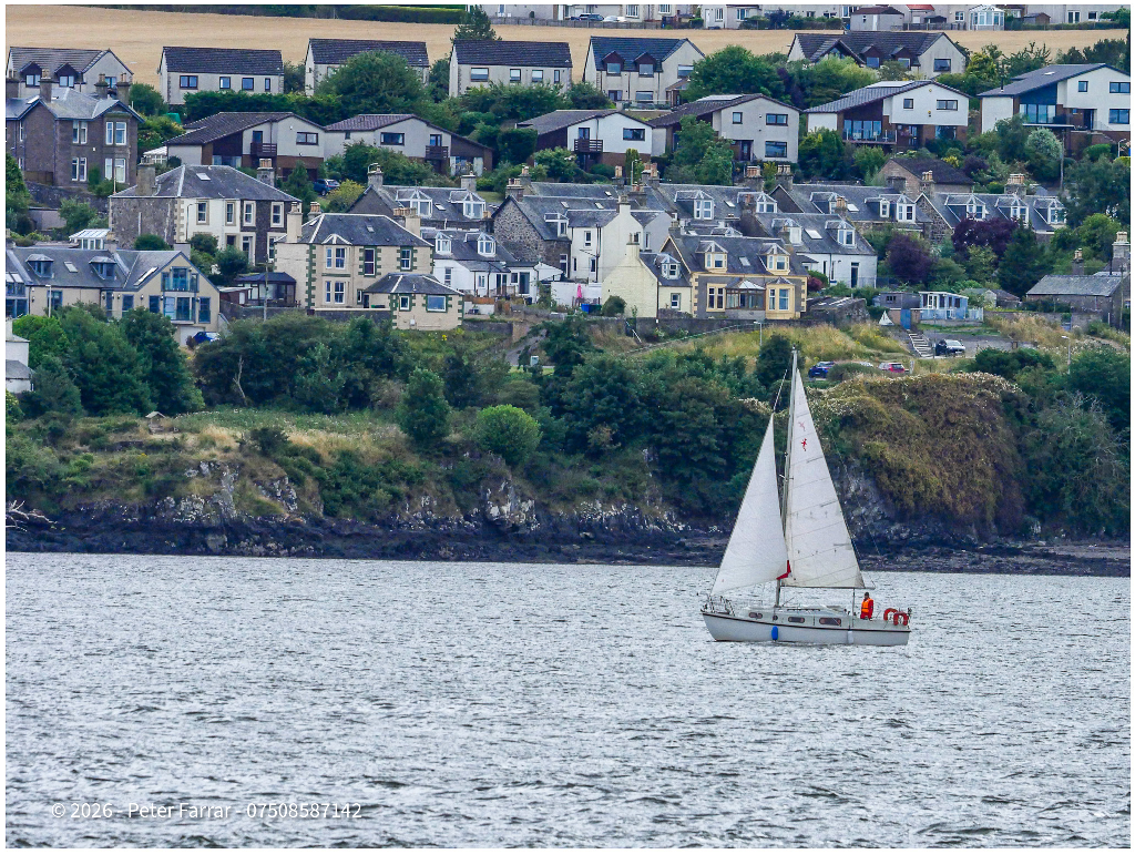 Sailing boat on calm water below a hillside village in Scotland showing the hyper focus used for sharp front to back.